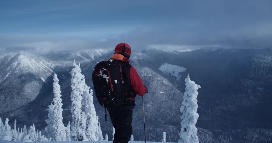 A person wearing cold weather gear stands in the snow while overlooking a mountain range
