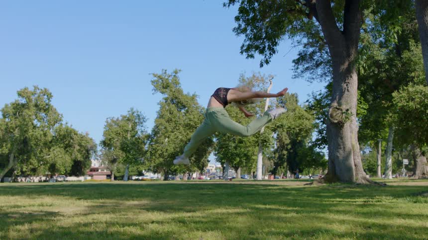 A woman does a dramatic spin in the air while dancing in a field during the day