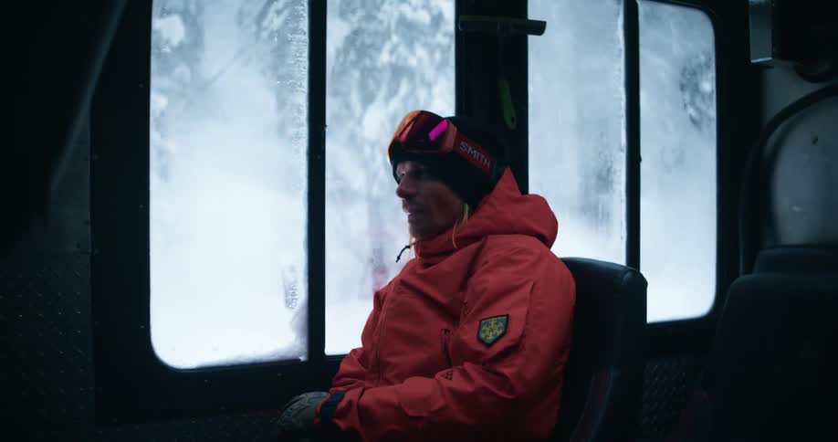 A man wearing winter gear is seated inside a train going through the winter snow