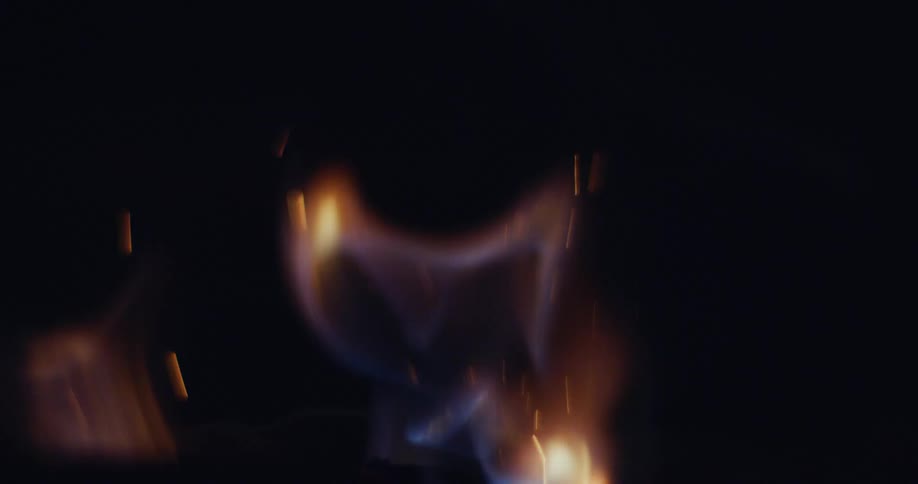 A fire burns in the darkness and releases sparks into the air