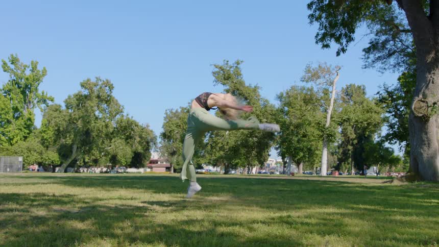 A woman is dancing outdoors in a field of grass