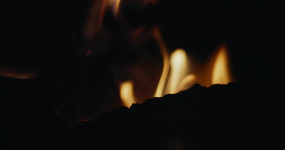 Flames consume the wood as a fire burns in the darkness of night