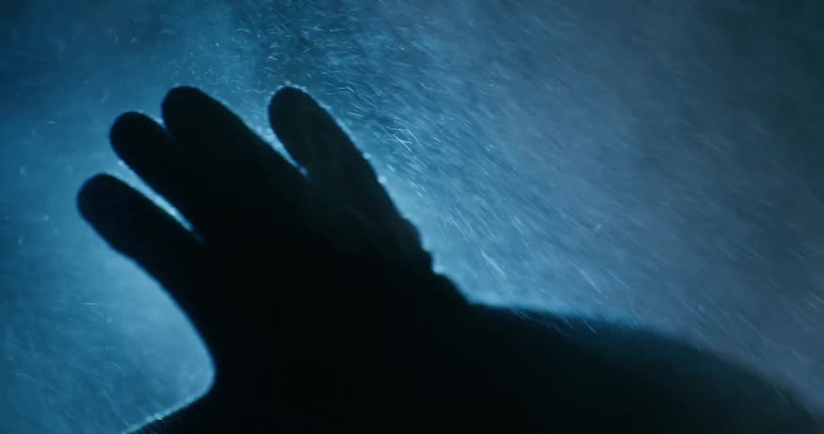 A person holds out their gloved hand while snow falls at night