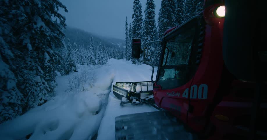 Red snow removal vehicle clearing a road next to trees and a mountain in winter
