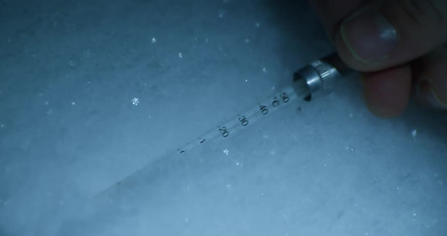 A person sticks a thermometer into the snow