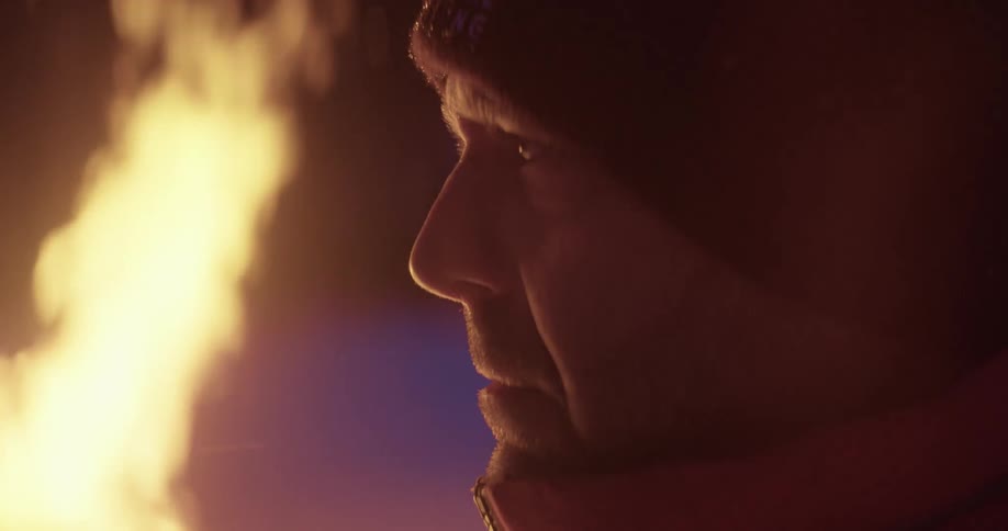 A sad and depressed man wearing a hat and jacket seeking warmth from the freezing weather as he stands near a fireplace
