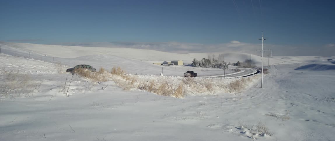 Large field with snow and a road with cars driving