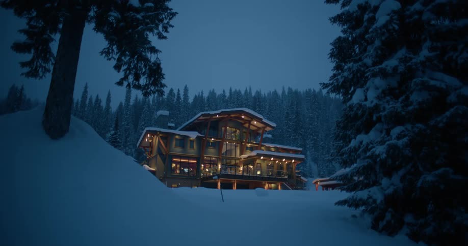Building in winter woods welllit surrounded by snow and trees at dusk