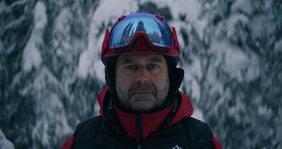 A man wearing cold weather gear stands near a snow covered forest