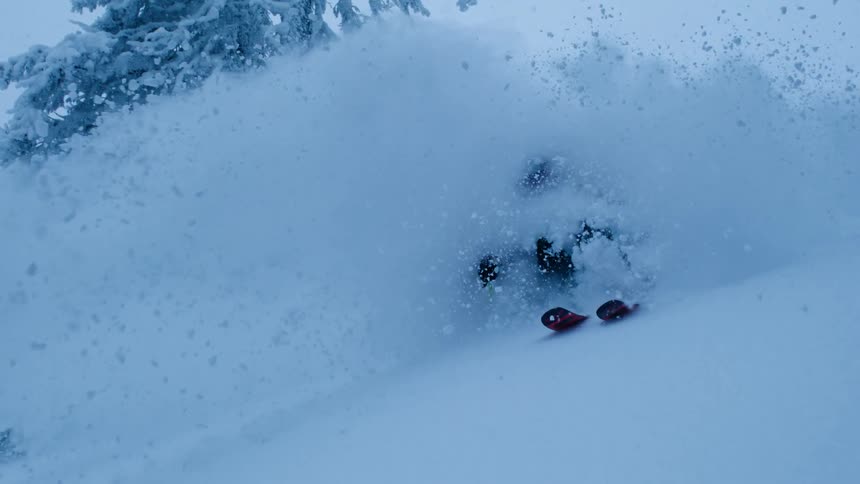 A skier skies through a cloud of snow on a mountain slope during the day