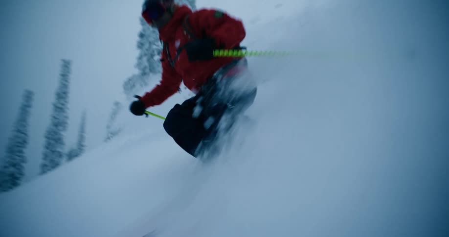 A skier sends up clouds of snow while skiing down a mountain slope on a cloudy day