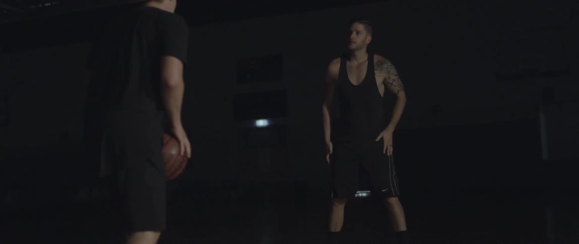 Men play basketball in a dark gymnasium