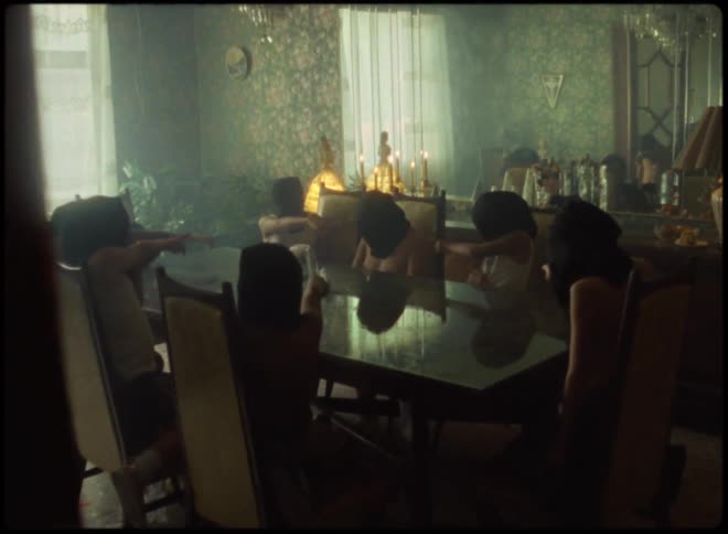 A small group of kids with black head covering point at one child while sitting at a table
