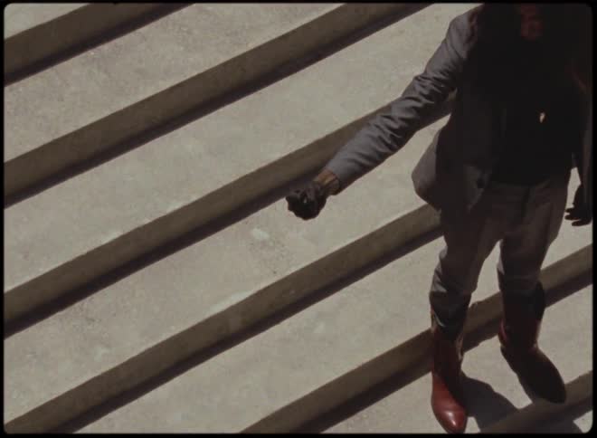 Person stands outdoors on path made of parallel slabs of concrete and makes a fist