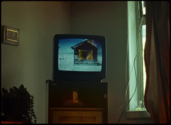 A television in a living room shows a burning house in the snow