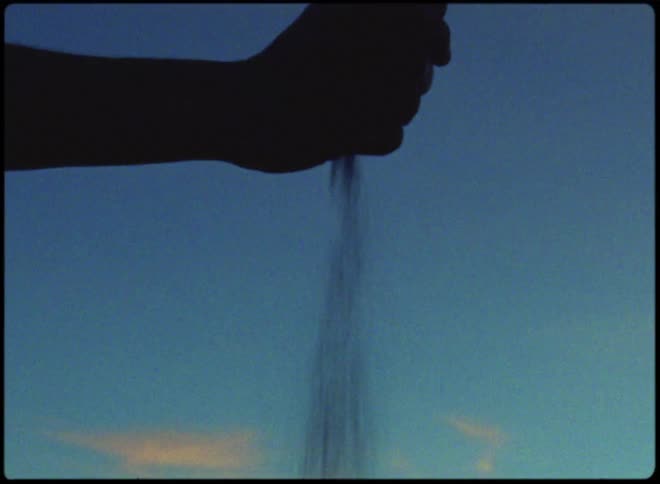 During sundown a person pours out sand held on hisher right hand