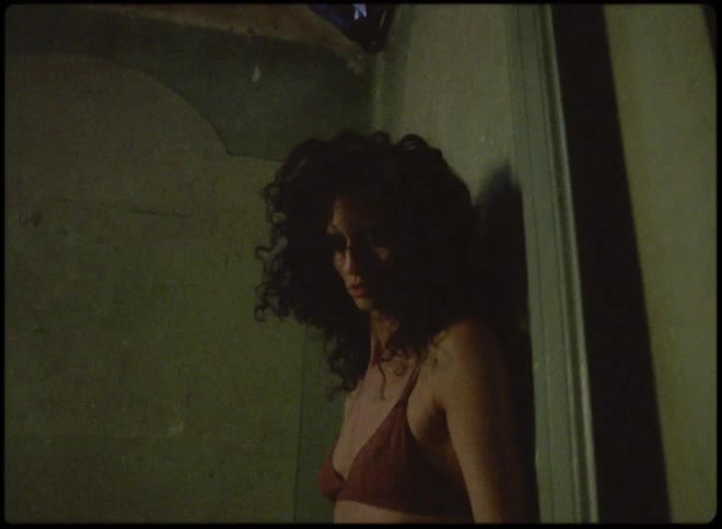 A sad looking person wearing a bra leans their head back against a dingy wall
