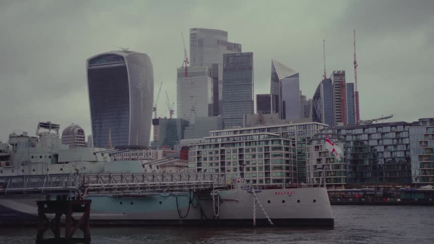 A military warship is docked near a metropolitan city with many skyscrapers