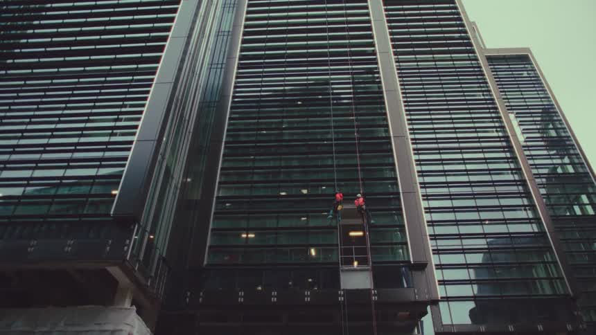 Two workers suspended in mid air working on a window in a skyscraper building