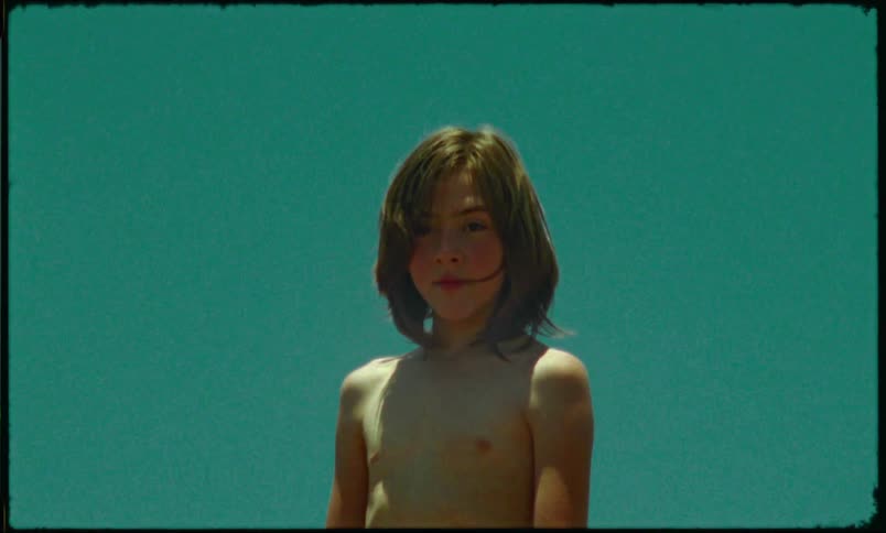 A young boy is shirtless in a rocky terrain with paint on his face