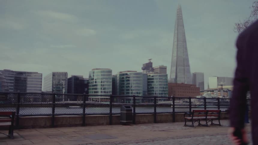 Businessman walks along path through park across river from mid rise buildings
