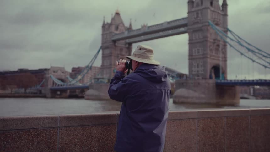 Male photographer takes pictures standing near river with london bridge in the background