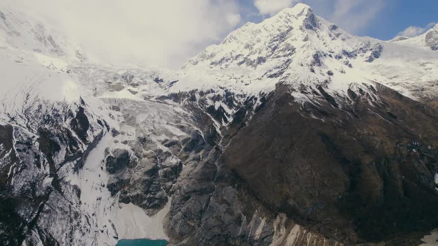 A turquoise lake at the base of a snow covered mountain range in the middle of the day