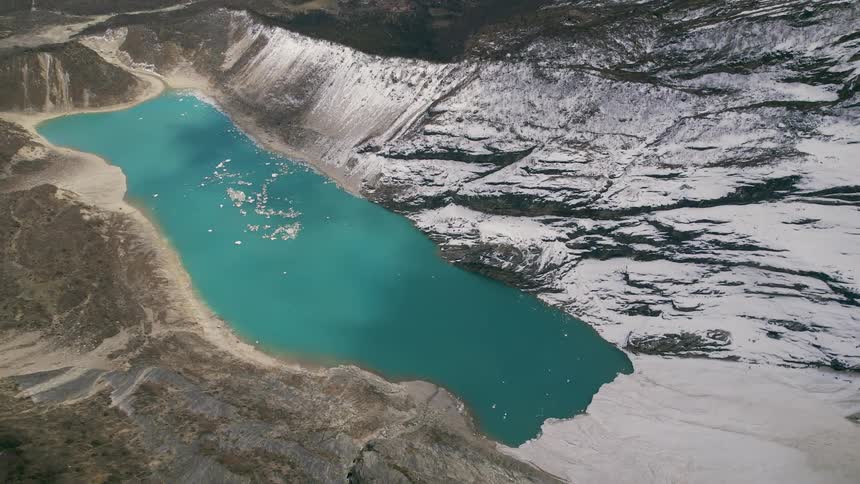 Vivid blue of mountain lake contrasts with white of snow