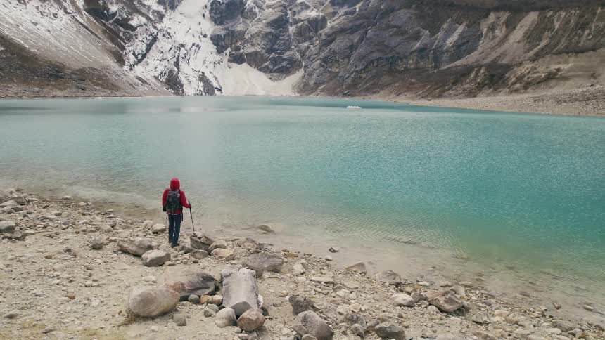 A man hikes next to a lake and stops and looks up at the mountain range around him