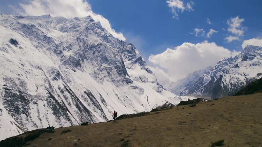 A hiker walks along a ridge near an enormous snowcovered mountain