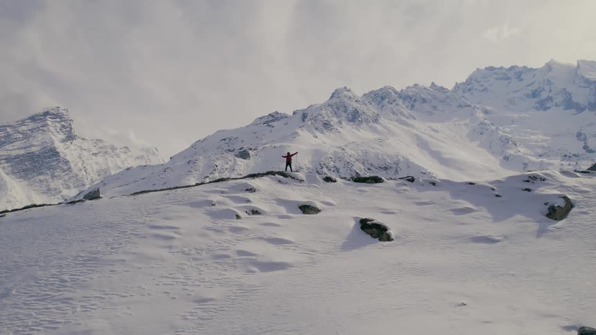 Person standing atop snowy mountain spreading arms in excitement during winter