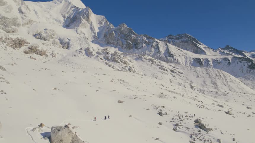 A group of mountaineers cross a snowy mountain slope during the day