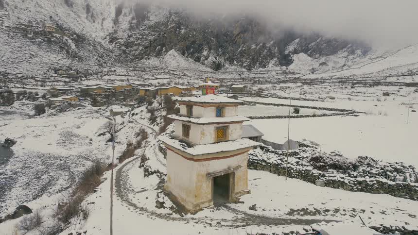 Paths lead through and past gate tower paralleling river on route to snow covered town nestled against mountain