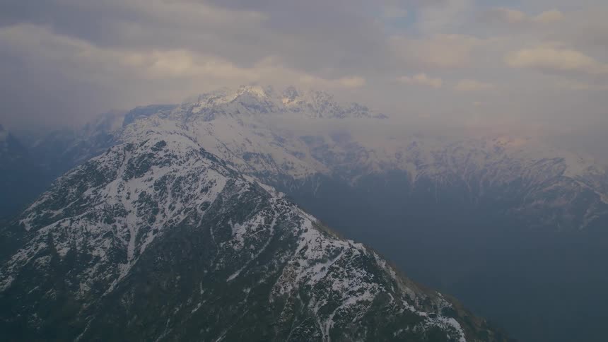 Snow covered mountain ridge rises above fog near cloud layer