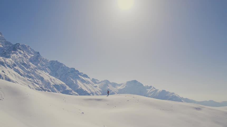 Person hiking up snowcovered hill towards mountains top in winter