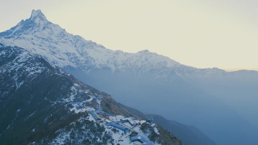 Buildings at mountains peak surrounded by green vegetation with some areas covered in snow