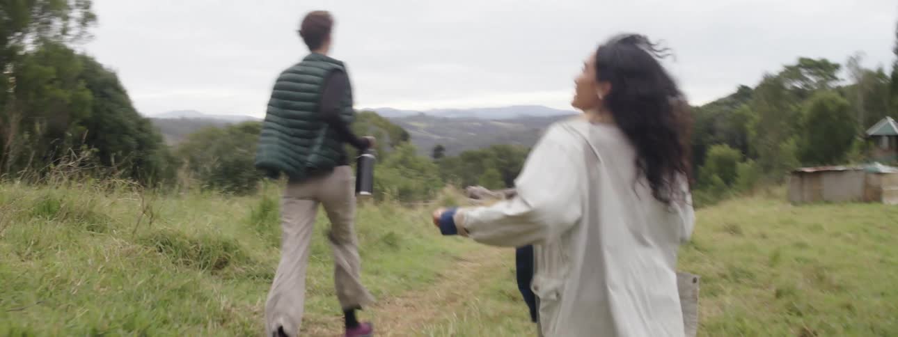A trio of people and a dog run through a grassy field near a valley