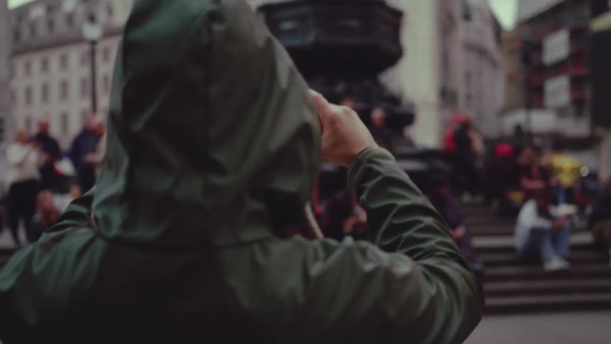 A man uses his phone to record a crowd sitting on steps in a city intersection