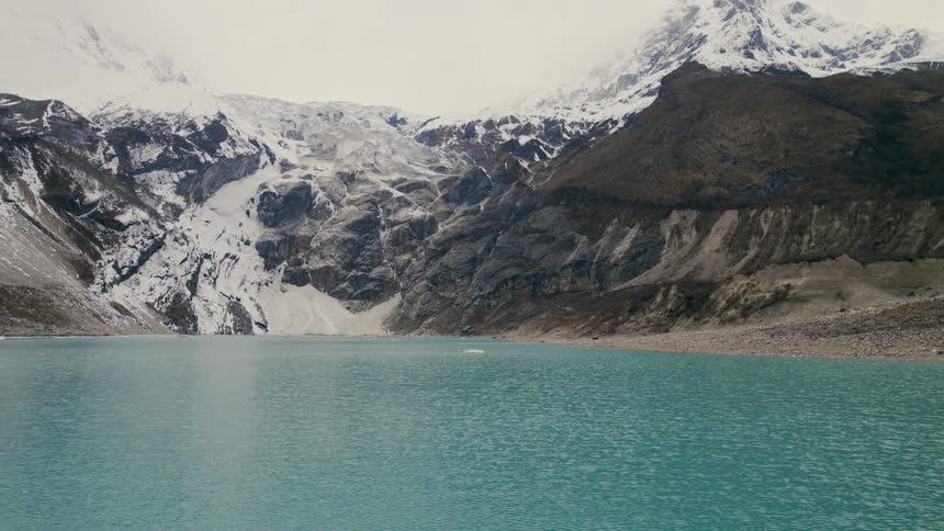 A river looking blueish flowing close to a mountain covered in snow