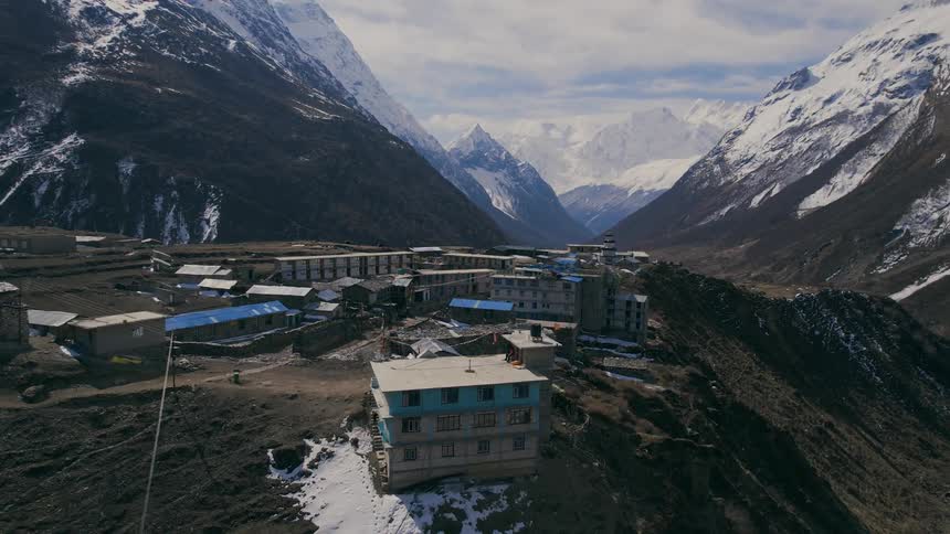 Buildings on a clearing in a mountain range surrounded with snow capped mountains
