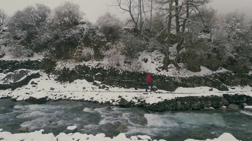 Hiker with red coat backpack and hiking poles walks by river