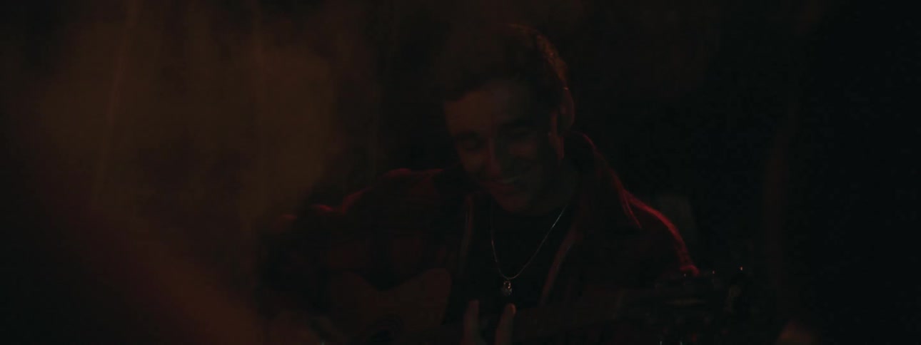 Happy man plays acoustic guitar under red lights on a party