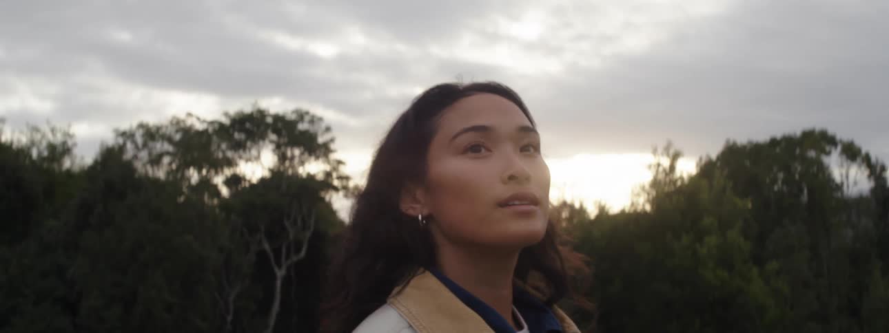 A woman looks up at the sky while standing outside the woods