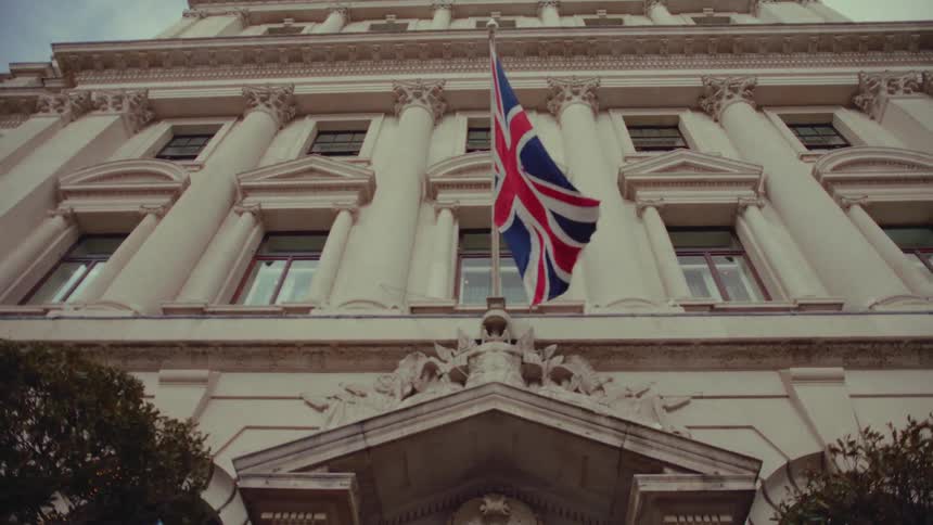 British flag flutters over entrance to building with neoclassical architecture
