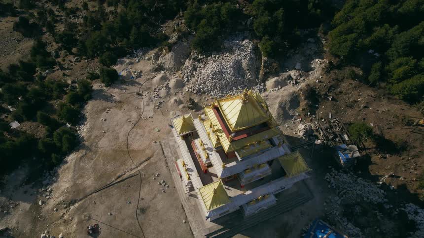 Aerial of an asian style building standing alone in the middle of the day with piles of rocks around it