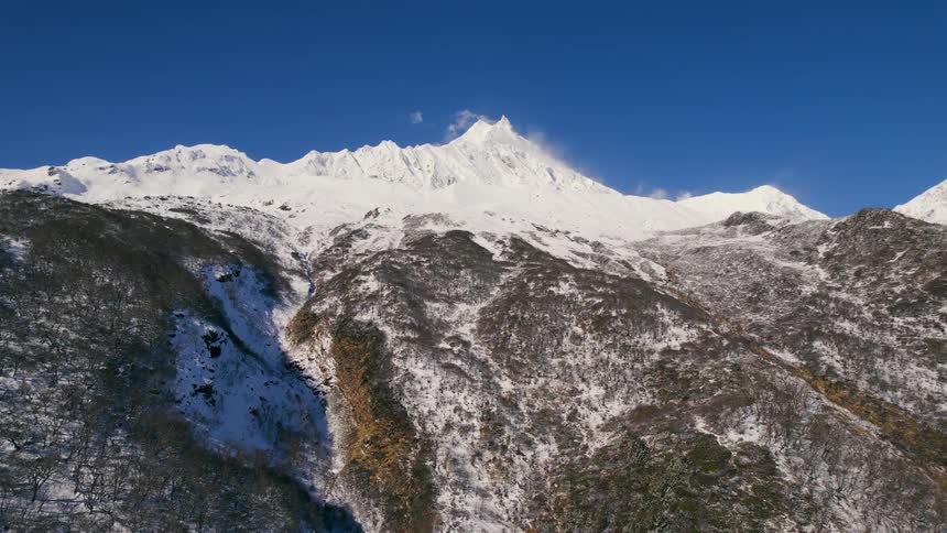 A snow capped mountain towers over a forest covered canyon