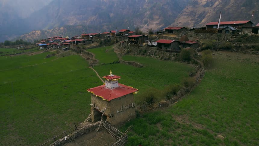 Banners flutter on tower decorated with face at edge of red roofed village in mountains