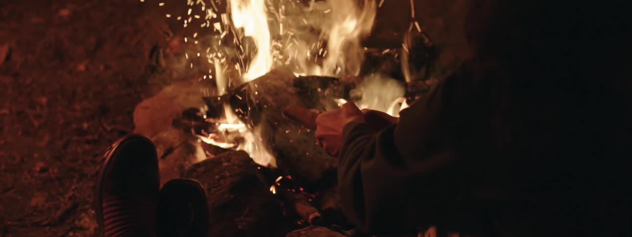 Hands of a man arranging logs on a burning campfire at night