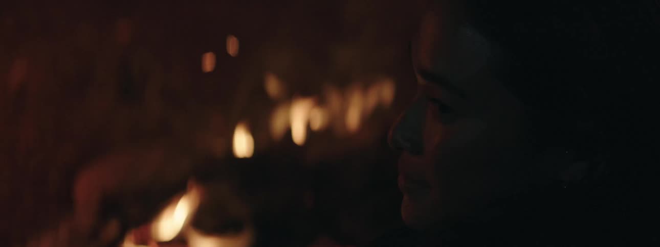 In the cold night a woman sit in a fireplace warming herself as she spread her fingers towards the fire