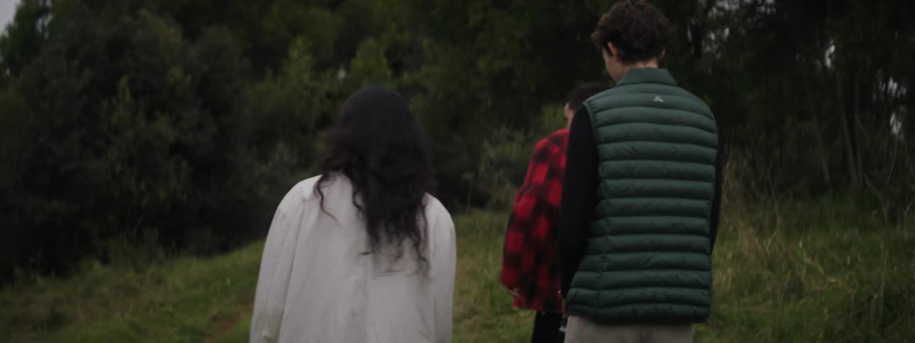 A teenage girl looks around a forest as she walks with two teenage boys one who is laughing